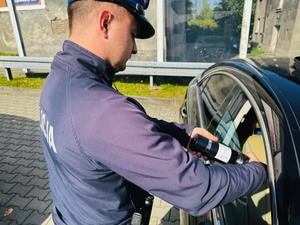 policjant sprawdzający przepuszczalność światła przez szybę w drzwiach specjalnym urządzeniem