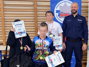 dzieci z dyplomami stoją wraz z komendantem komisariatu po finale zawodów tenisowych